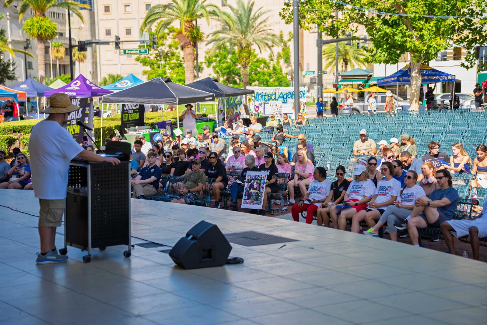 A speaker addresses a seated crowd from the Walk for Lives stage in Orlando